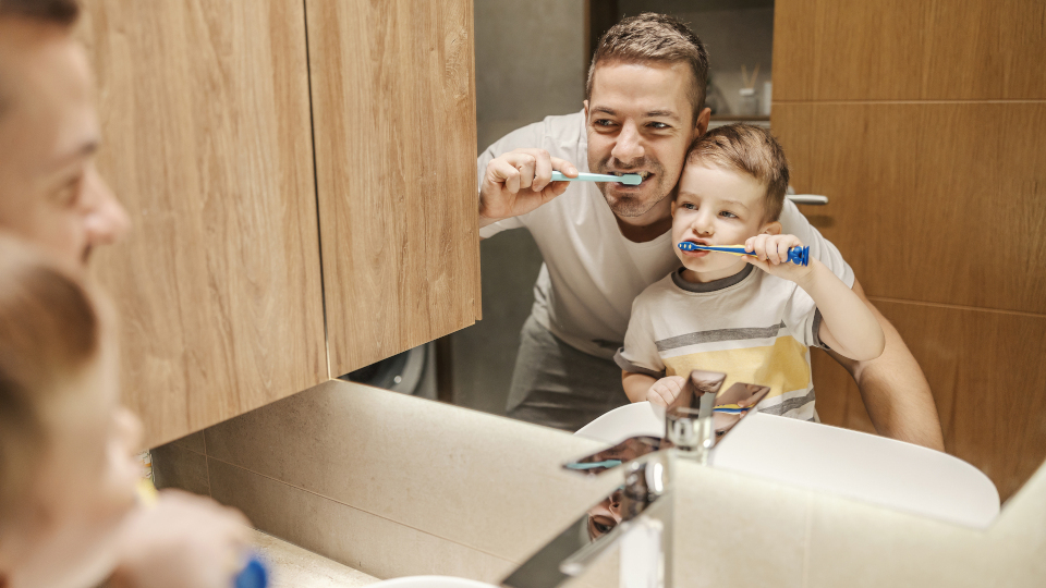 Ein Vater zeigt seinem Sohn richtiges Zähneputzen.