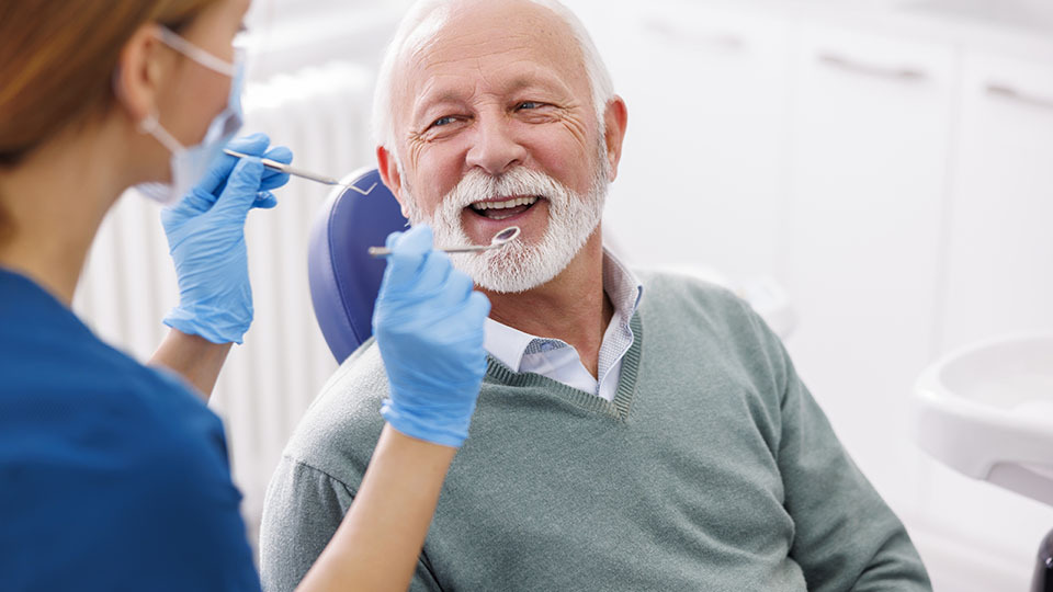 Auswirkungen von Diabetes auf Zahngesundheit: Älterer Mann sitzt lächelnd auf Zahnarztstuhl