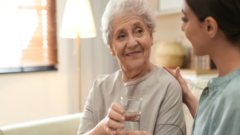 Eine junge Frau reicht einer älteren Dame ein Glas Wasser